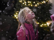 Serena Brown, 8, closes her eyes as snowflakes from a snow machine fall on her face Friday at Activate Church’s sixth annual Christmas at the Park in Esther Short Park. Below: Yesenia Alcazar, left, helps her children, Marley Compos, 2, left, and Damian Campos, 9, decorate Christmas cookies.