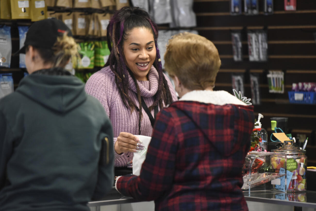 Kayzla Worlitz, assistant manager at Sticky’s Pot Shop in Hazel Dell, hands a customer a bag of the store’s merchandise on Wednesday. The shop remains open, despite a county ban, while the law is contested in the courts.