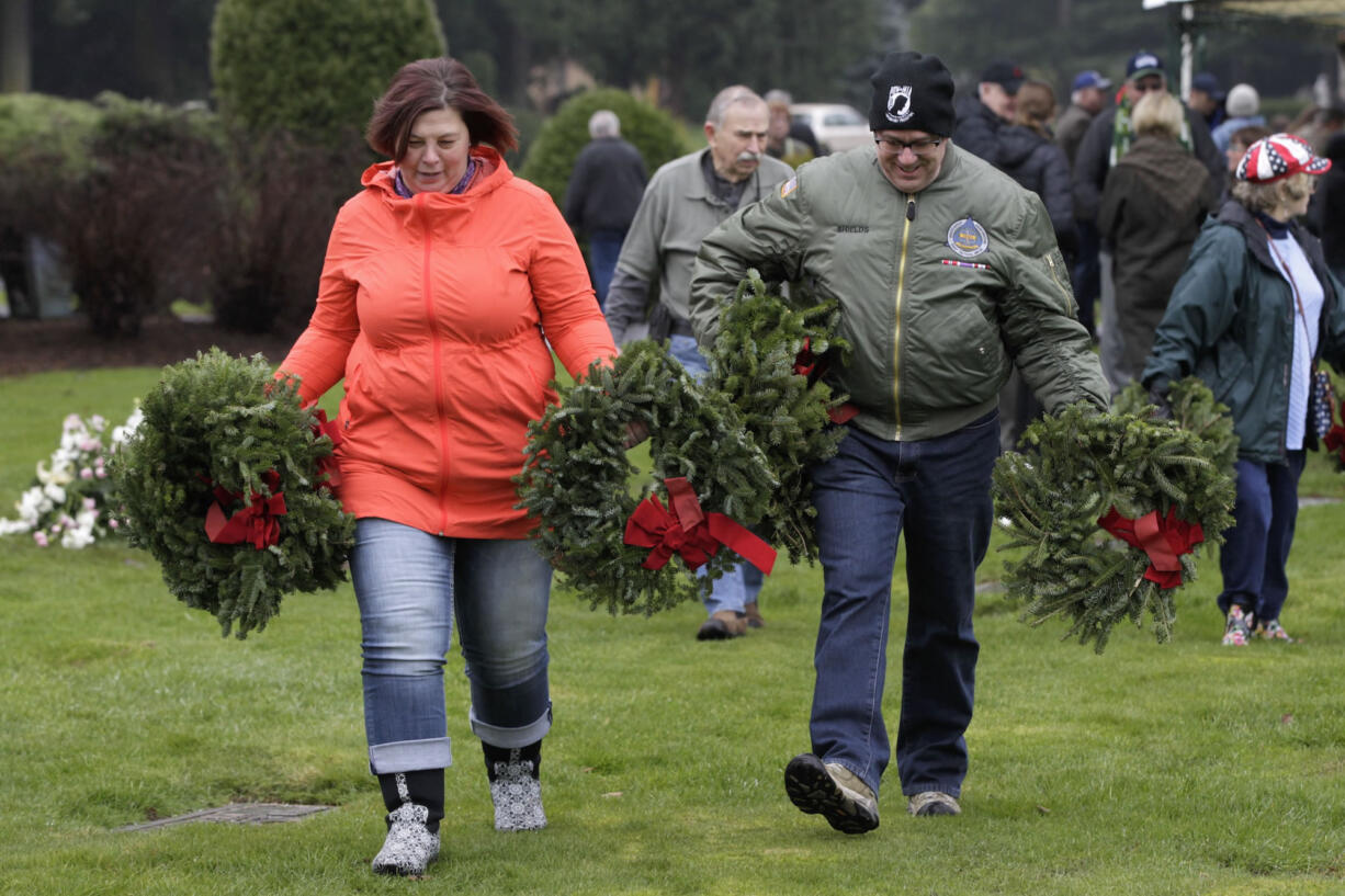 Carol, left, and John Shields carry wreaths to place on military graves at Evergreen Memorial Gardens as part of the Wreaths Across America activities Saturday.