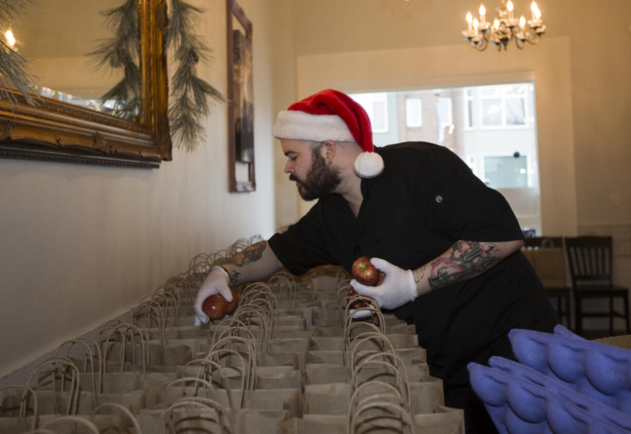 Brandon Dickover places apples in bags to be donated to the needy on Christmas Day at Bleu Door Bakery on Monday.