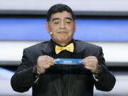 Argentine soccer legend Diego Maradona holds up the team name of Spain at the 2018 soccer World Cup draw in the Kremlin in Moscow, Friday, Dec. 1, 2017.