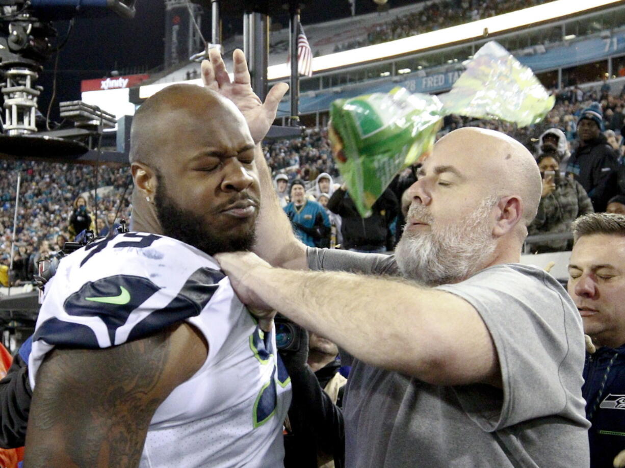 A Seattle Seahawks staff member tries to remove Seahawks defensive tackle Quinton Jefferson, left, from the field as an object thrown from the stands hits them during the closing moments of an NFL football game against the Jacksonville Jaguars, Sunday, Dec. 10, 2017, in Jacksonville, Fla. Jacksonville won 30-24. (AP Photo/Stephen B.