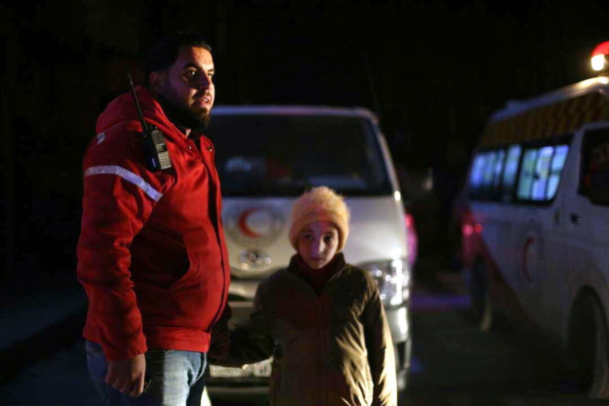 A member of the Syrian Arab Red Crescent stands with a girl during a human evacuation of sick people from the eastern Ghouta, near Damascus, Syria, Wednesday, Dec. 27, 2017.