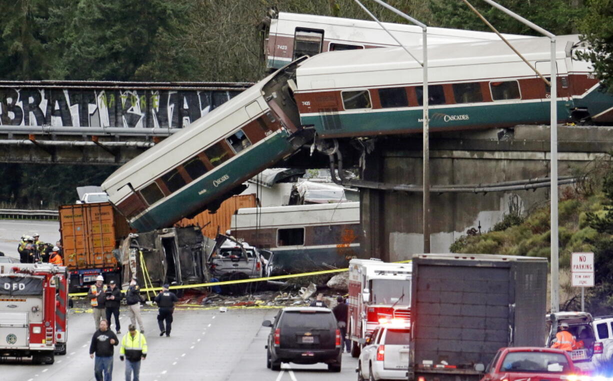 FILE - In this Dec. 18, 2017, file photo, cars from an Amtrak train lie spilled onto Interstate 5 below alongside smashed vehicles as some train cars remain on the tracks above in DuPont, Wash. Federal investigators say video aboard the Amtrak train that derailed in Washington state shows crews weren’t using personal electronic devices and that the engineer remarked about the speed six seconds before the train went off the tracks south of Seattle.