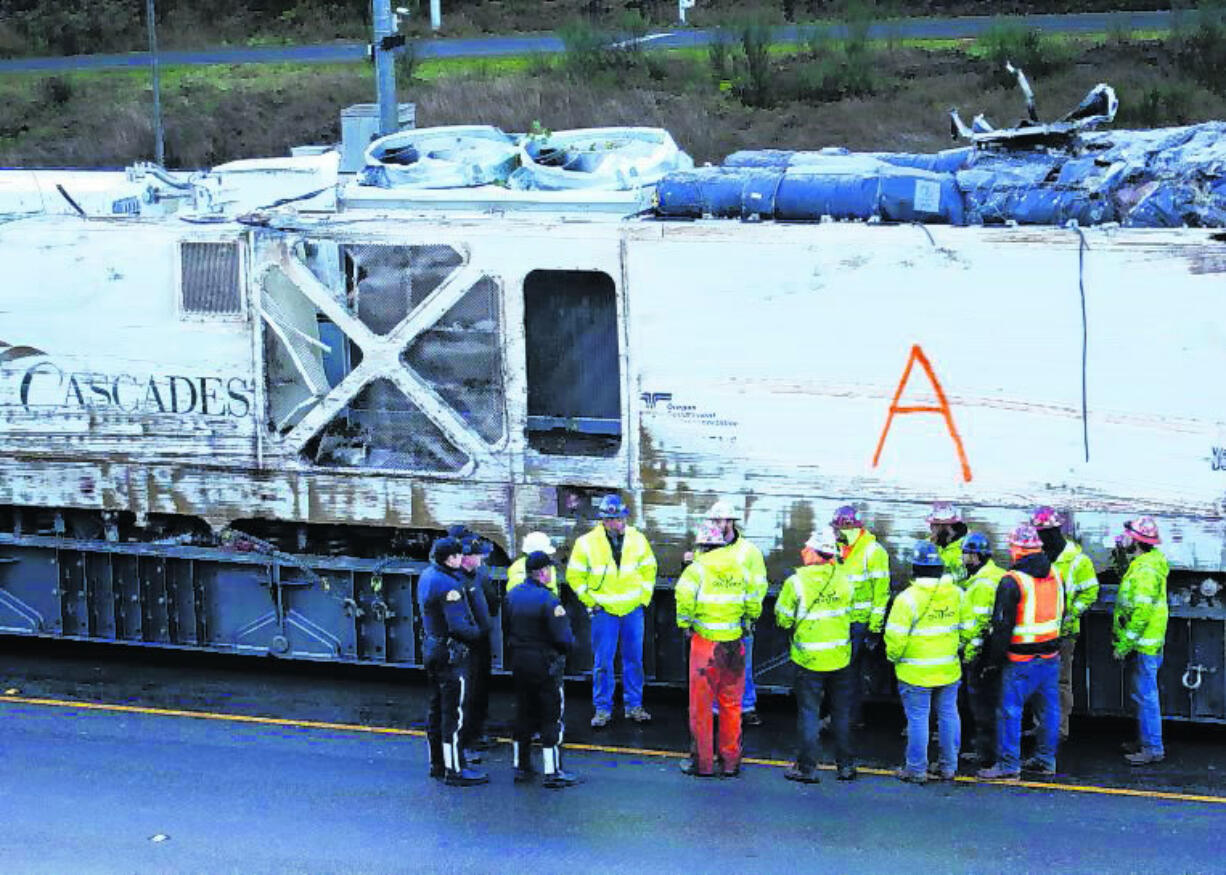 State Patrol officers and workers gather before transporting the engine from an Amtrak train crash two days earlier away from the scene, Wednesday, Dec. 20, 2017, in DuPont, Wash. The Amtrak train that careened off the overpass south of Seattle, killing at least three people, was hurtling 50 mph over the speed limit when it jumped the track, federal investigators say, when it derailed along a curve, spilling railcars onto the highway below.