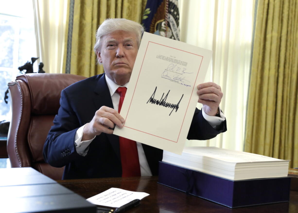 President Donald Trump holds up a page of the $1.5 trillion tax overhaul package he signed Friday in the Oval Office.