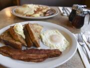 French toast with bacon and an over-easy egg are offered at The Plainsman Restaurant. Biscuits and gravy with hash browns and sausage are seen in the background.