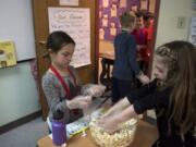 King’s Way Christian Schools first-graders Meah Carlson, left, and Cali Creagan, right, pack bags full of popcorn to sell Thursday during the marketplace section of the school’s new yearlong MicroSociety project. The curriculum puts students in charge of running a country over the course of the year.