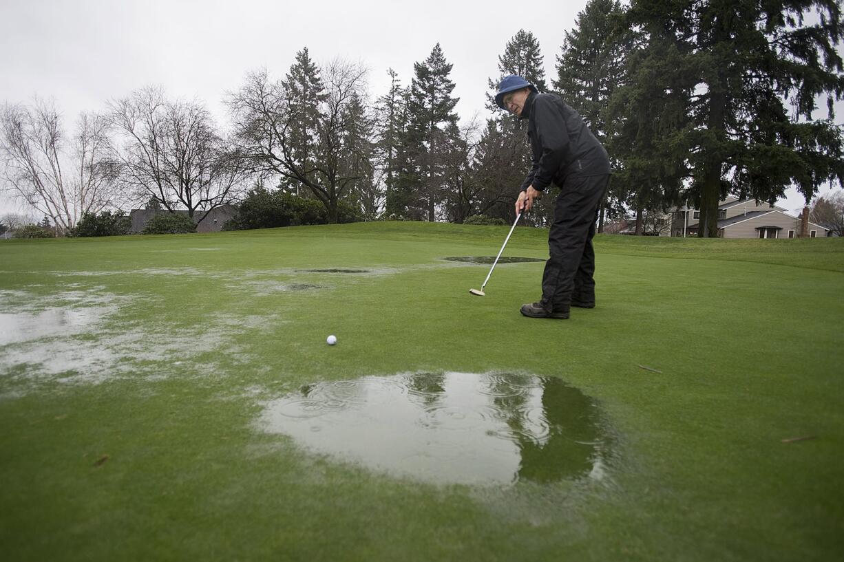 Jim Mewhirter of Vancouver attempts to putt around puddles on the first hole during a rainy golf game at Fairway Village on Thursday morning.