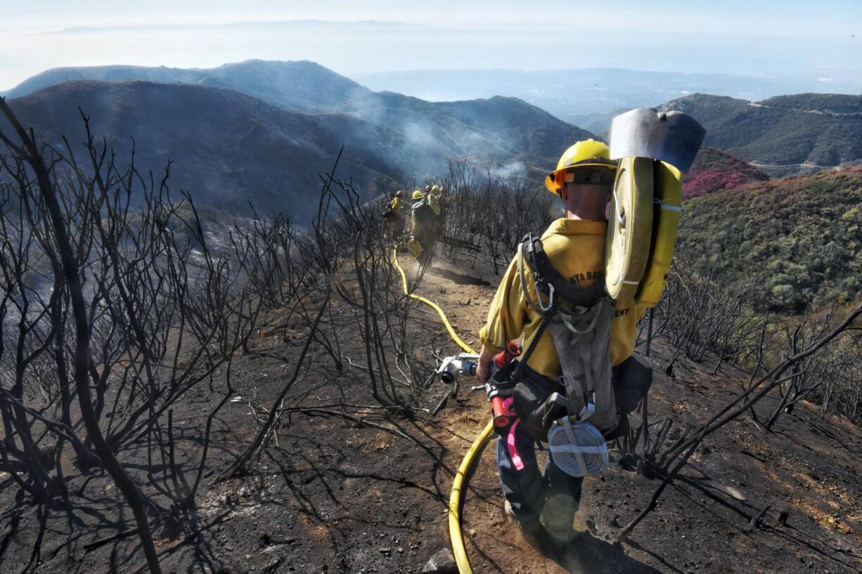 FILE - In this Dec. 19, 2017 file photo provided by the Santa Barbara County Fire Department, Santa Barbara County Firefighters haul dozens of pounds of hose and equipment down steep terrain below E. Camino Cielo to extinguish smoldering hot spots in Santa Barbara, Calif. Evacuations have been ordered for communities below hillsides charred by California's largest-ever wildfire as the first major winter storm of the season brings rare rain and raises the risk of mudslides.