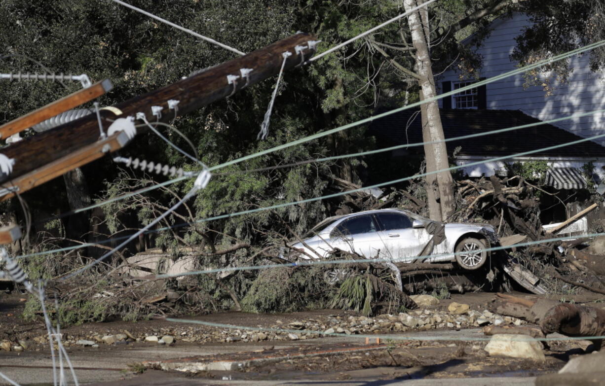 A damaged car sits over fallen and debris behind downed power lines in Montecito, Calif. While an aggressive cleanup could mean Montecito will welcome visitors again in weeks, the rebuilding of infrastructure and hundreds of homes will be measured in months and years. It will also offer a chance to re-imagine aspects of a town that has favored slow growth over the runaway development closer to Los Angeles, 90 miles down the coast.