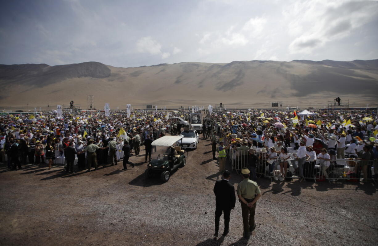 Security looks on as Pope Francis rides on a pope-mobile past the crowd as he arrives to celebrate Mass on Lobito Beach in Iquique, Chile, on Thursday. Pope Francis urged the people to continue to be welcoming toward migrants in this Chilean coastal city which has experienced a boom of immigrants from several countries.