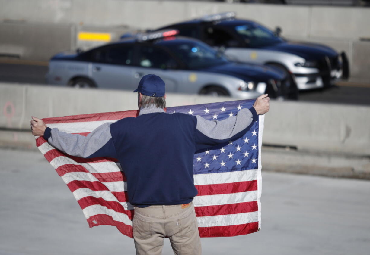 David Morgan of Highlands Ranch, Colo., holds an American flag as a procession of law enforcement vehicles accompany a hearse carrying the body of a sheriff’s deputy shot and killed while responding to a domestic disturbance Sunday, Dec. 31, 2017, in Highlands Ranch, Colo.