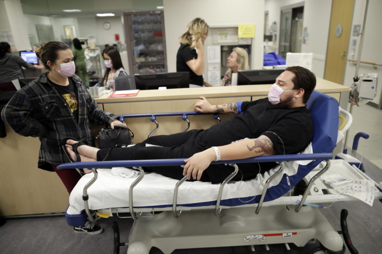 Donnie Cardenas, right, waits in an emergency room hallway alongside roommate Torrey Jewett, left, as he recovers from the flu at the Palomar Medical Center in Escondido, Calif., on Wednesday, Jan. 10, 2018. The San Diego County resident said he was battling a heavy cough for days before a spike his temperature sent him into the emergency room.