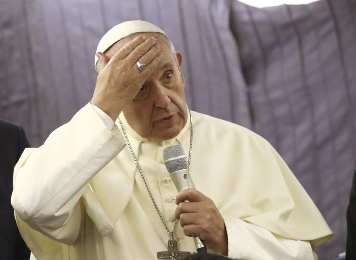 Pope Francis touches his forehead as he talks with journalists during his flight from Lima, Peru, to Rome on Sunday.