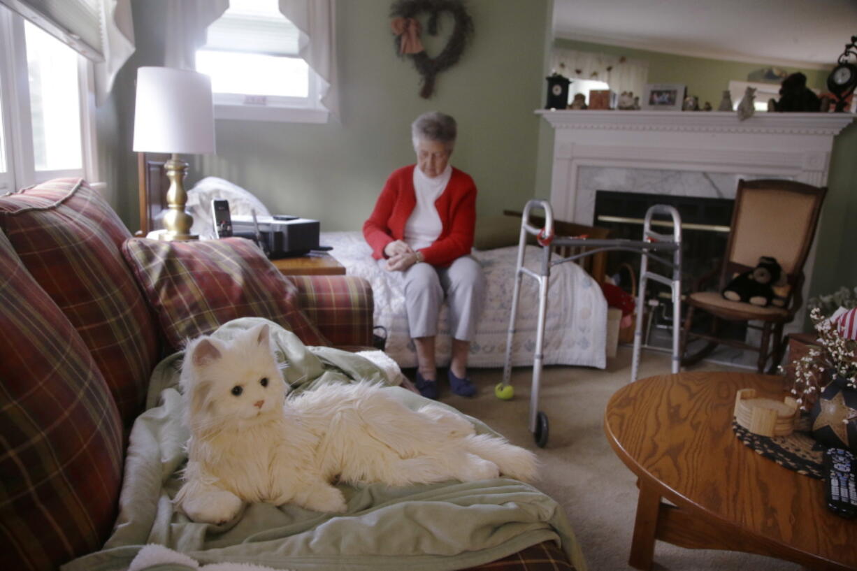 In this Friday Dec. 1, 2017, photo, 93-year-old Mary Derr sits on her bed near her robot cat she calls “Buddy” in her home she shares with her daughter Jeanne Elliott in South Kingstown, R.I. Buddy is a Hasbro’s “Joy for All” robotic cat, aimed at seniors and meant to act as a “companion,” it has been on the market for two years. Derr has mild dementia, and Elliott purchased a robot earlier this year to keep her mother company.