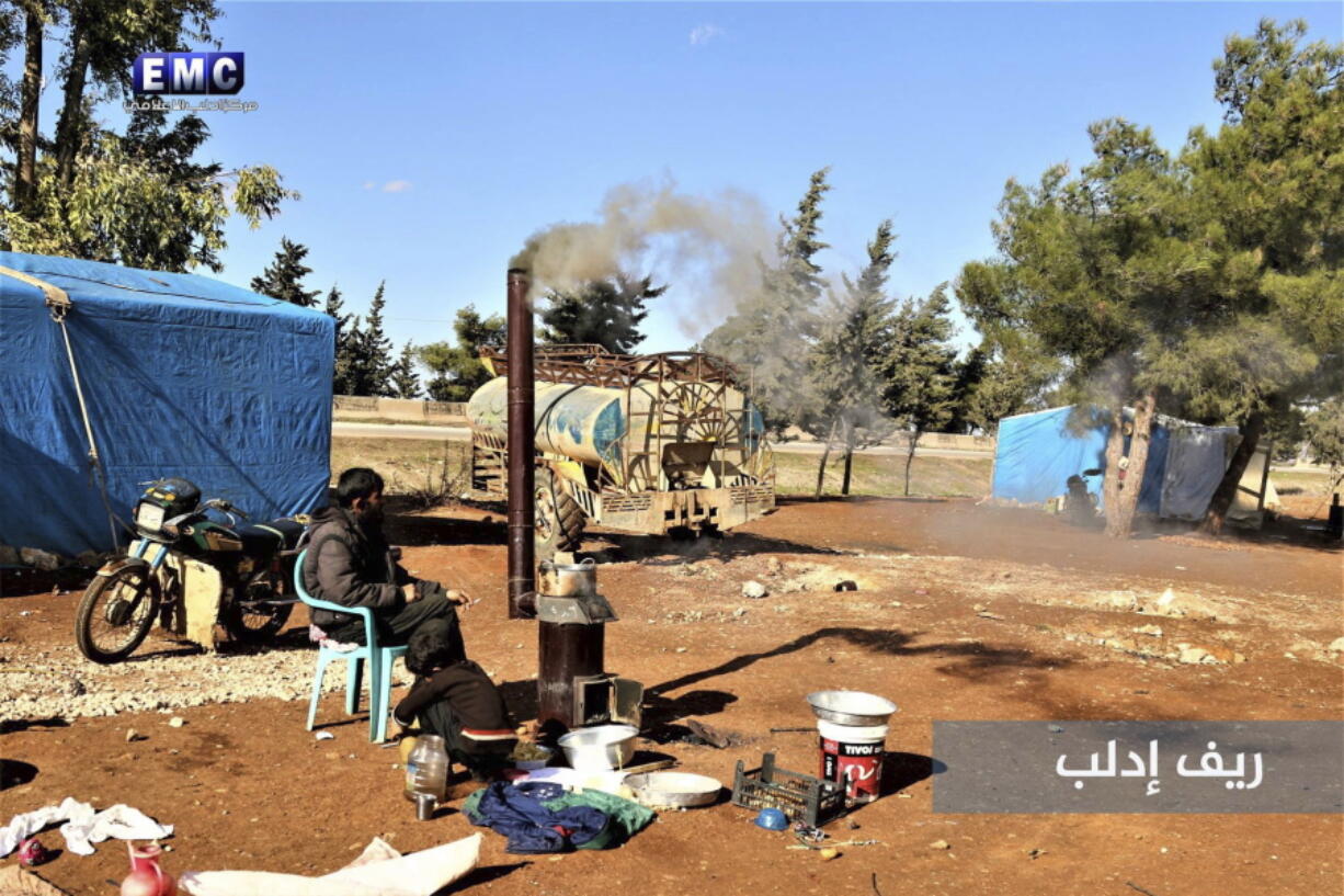 In this photo provided on Tuesday Jan. 2, 2018 by the Syrian anti-government activist group, Edlib Media Center, EMC, which has been authenticated based on its contents and other AP reporting, shows Syrian displaced man and boy who fled from a countryside village of Idlib city, which is under the attack of the Russian and Syrian government airstrikes, sits outside their tent at an informal refugee camp, near Idlib, Syria. Syrian government forces and allied militiamen are advancing on the largest remaining rebel-held territory in the country’s north, forcing thousands of civilians to flee toward the border with Turkey amid a crushing offensive just as the cold winter weather sets in.