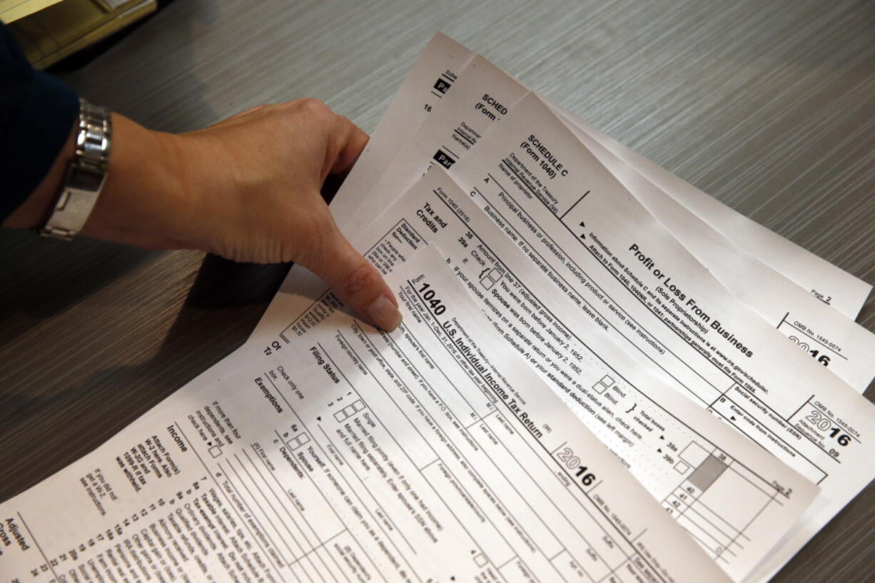 FILE - In this Jan. 14, 2017 file photo, tax professional and tax preparation firm owner Alicia Utley reaches for hard copies of tax forms while working to stay caught up at the start of the tax season rush in her offices at Infinite Tax Solutions, in Boulder, Colo. Millions of working Americans should start seeing fatter paychecks as early as next month, the IRS says, as a result of the recently passed tax law.