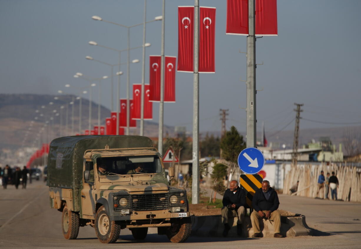 A Turkish Forces vehicles is driven past people watching at the Oncupinar border crossing with Syria, known as Bab al Salameh in Arabic, in the outskirts of the town of Kilis on Monday. Renewed clashes erupted on Monday on a strategic hilltop in northwestern Syria captured by Turkish troops the day before as Syrian Kurdish militiamen try to regain control.