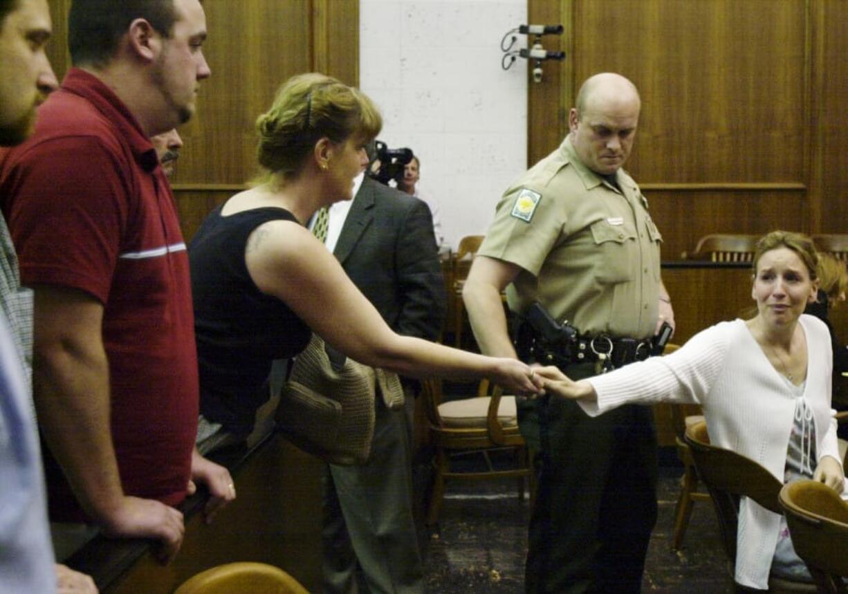 Heidi Fero, right, looks at her then-fiancé, Dustin Goodwin, partially visible at far left, as she hands her jewelry to her mother, Joan Fero, following sentencing on May 2, 2003.