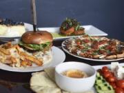 Offerings from Luxe include, clockwise from left, a Gorgonzola burger with Parmesan garlic fries, a slice of blueberry lemon curd cheesecake, crab cakes, a Margherita pizza and the hummus plate.