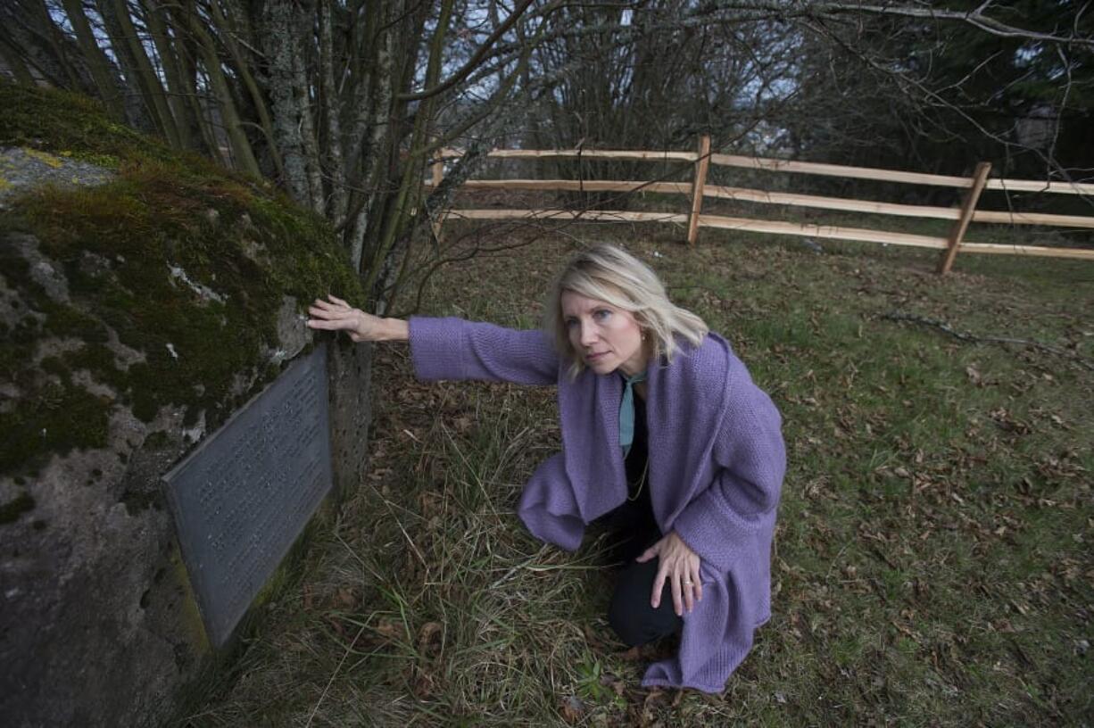 Lisa Bayautet kneels next to a marker noting that while people buried in the poor farm died in poverty, they helped settle the area.