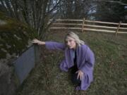 Lisa Bayautet kneels next to a marker noting that while people buried in the poor farm died in poverty, they helped settle the area.