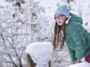 Eden Stahley, 9, leans over a snow-covered fence to look into a marsh at Mount Vista near WSU Vancouver, Monday morning, February 19, 2018. Stahley and her two sisters were enjoying the few inches of snow by sledding together on a hill near their home.