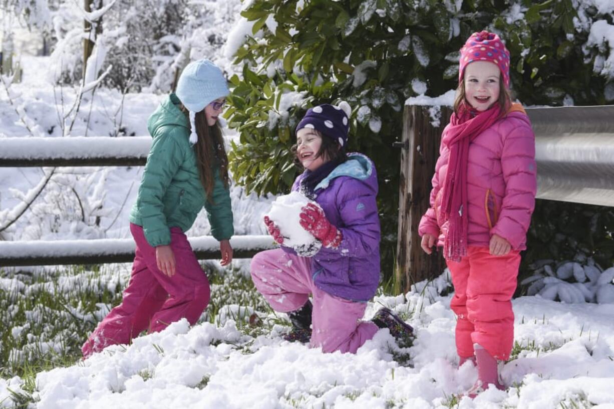 Eden Stahley, 9, from left, plays with her sister, Elliette Stahley, 7, while Esme Stahley, 5, looks toward her mom during a snowy day Monday morning. The family lives in the Mount Vista neighborhood near Washington State University Vancouver, where overnight snow lingered into midday. The sisters had been enjoying the winter weather by sledding together on a hill.