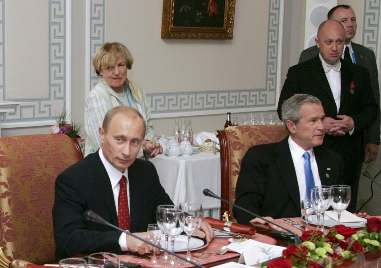 FILE - In this Monday, July 19, 2006 file photo, Russian President Vladimir Putin, left, and U.S. President George W Bush attend a working dinner with the other leaders of the G8 nations, as Russian businessman Yevgeny Prigozhin stands on the right, in St. Petersburg, Russia. While Russian officials have denigrated a U.S. indictment charging 13 Russians with meddling in the 2016 U.S. presidential vote through an elaborate social media campaign, former Internet trolls employed at the same facility see them as well-grounded. The indictment alleged that Yevgeny Prigozhin _ a wealthy entrepreneur and restaurateur dubbed "Putin's chef" _ funneled money to set up the troll factory that sent operatives to the United States, created fictitious social media accounts and used them to spread tendentious messages.