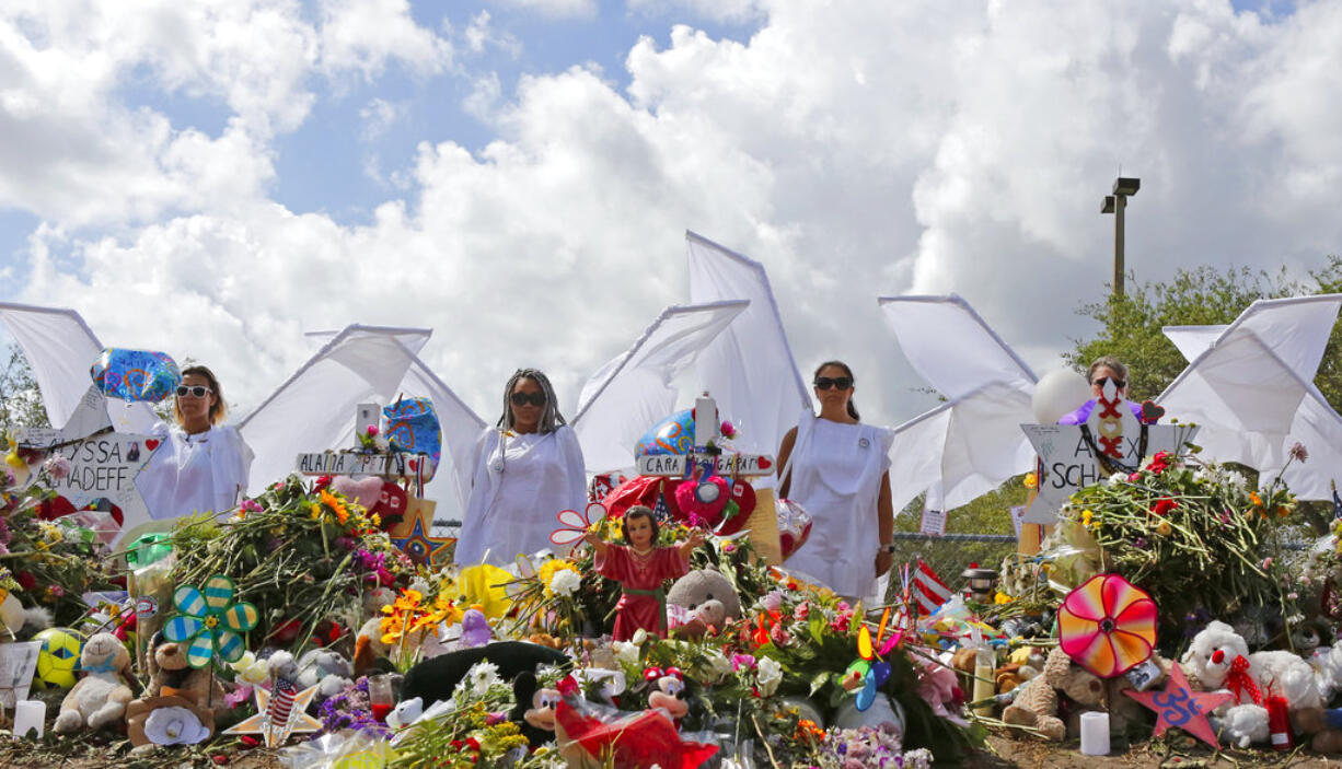 People dressed in white costumes as angels stand by a makeshift memorial outside Marjory Stoneman Douglas High School in Parkland, Fla., Sunday, Feb. 25, 2018. Thousands of students joined their parents in walking past the three-story building at the Florida high school where the Feb. 14 shooting took place. It is now cordoned off by a chain link fence that was covered with banners from other schools showing their support.