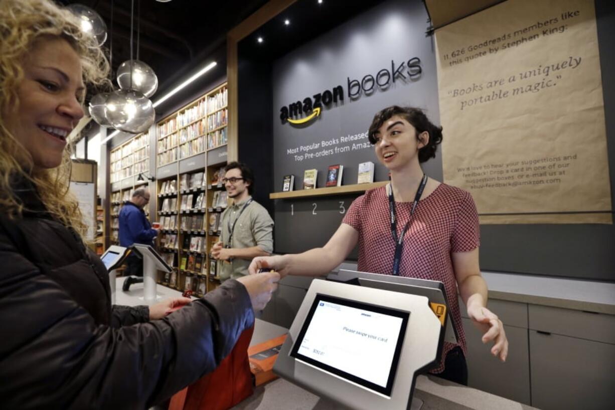 FILE - In this Nov. 3, 2015, file photo, customer Kirsty Carey, left, gets ready to swipe her credit card for clerk Marissa Pacchiarotti, as she makes one of the first purchases at the opening day for Amazon Books in Seattle. Amazon has opened more than a dozen locations of Amazon Books, which also sell some toys, electronics and Amazon gadgets.