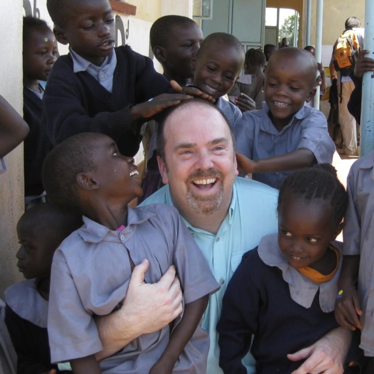 This 2011 photo provided by Greg Eubanks, CEO of an adoption agency in Washington state called WACAP, shows him surrounded by students from a community elementary school in Nairobi, Kenya. In 2018, Eubanks says his agency, and other U.S. adoption agencies dealing in international adoption, face difficulties ahead because of higher fees and tougher regulations being imposed by the U.S. State Department.