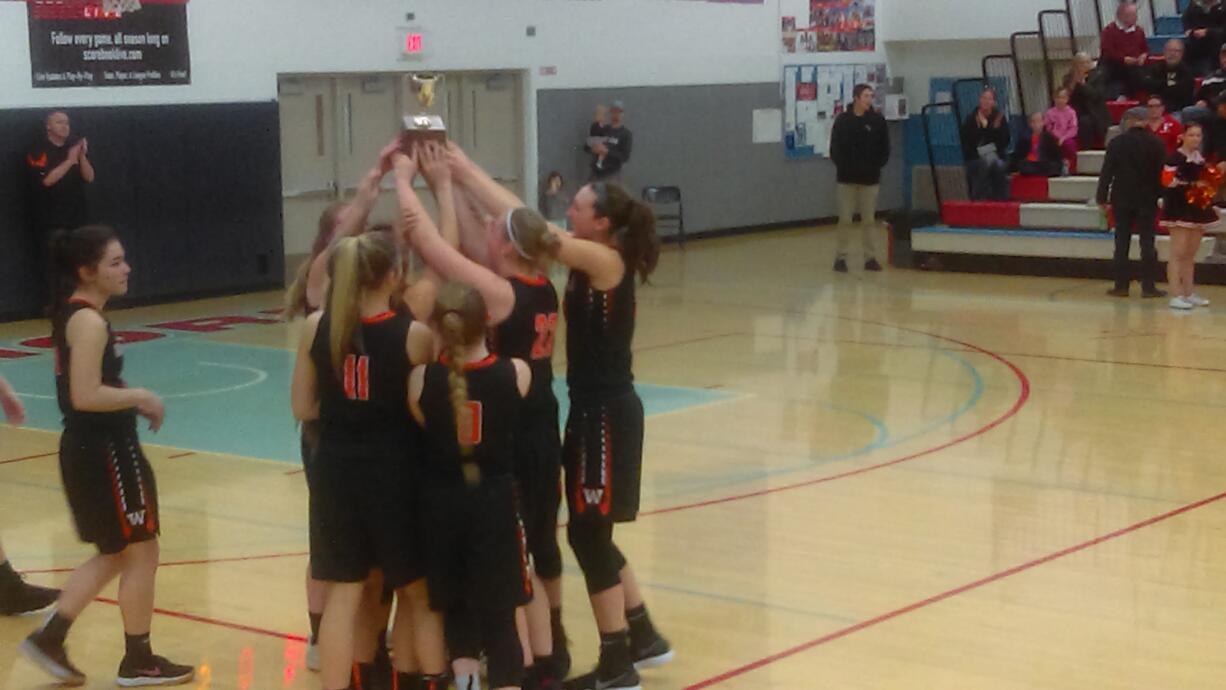 The Washougal girls basketball team hoist the third-place trophy at district after beating Woodland 52-36 (Tim Martinez/The Columbian)