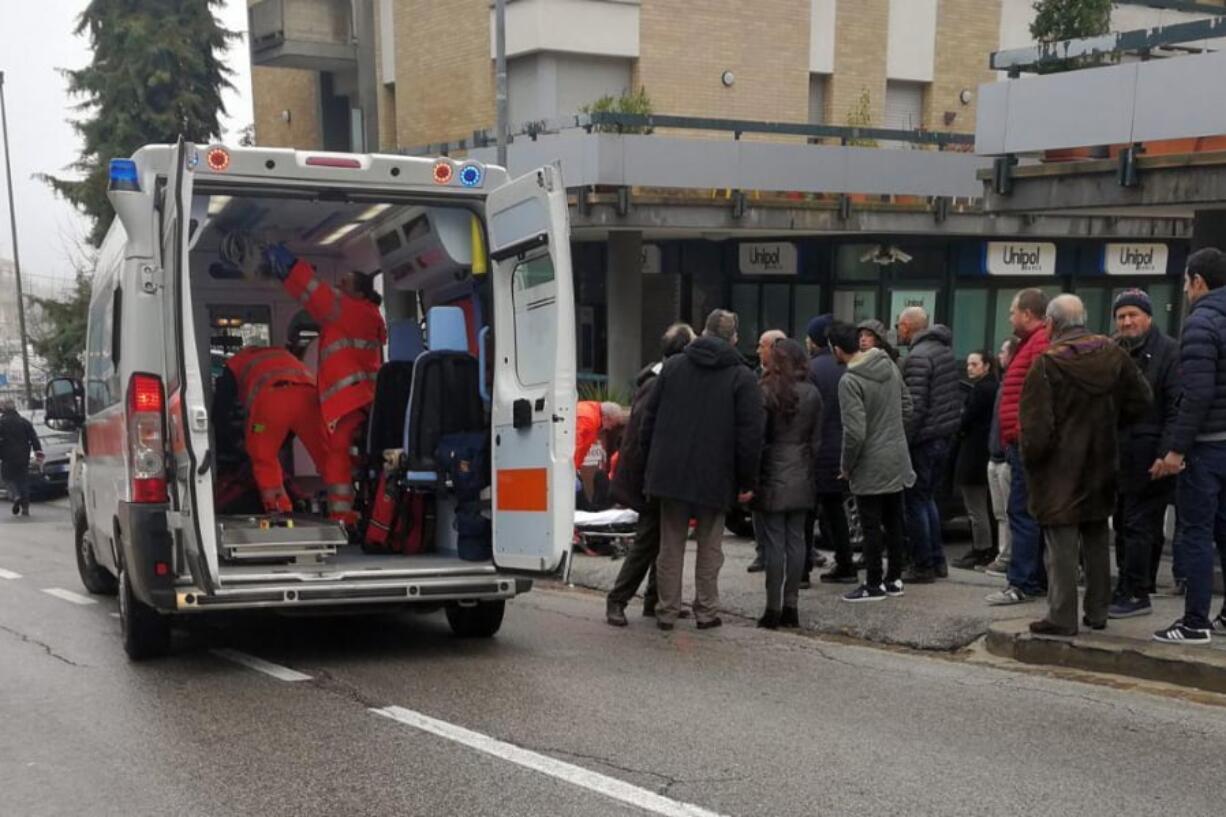 Paramedics, background center, attend a wounded man after a shooting broke out in Macerata, Italy, Saturday, Feb. 3, 2018. Italian police arrested a lone gunman in a series of drive-by shootings targeting foreigners Saturday morning that paralyzed a small central Italian city still reeling from the gruesome murder of a young Italian woman allegedly at the hands of a Nigerian immigrant.