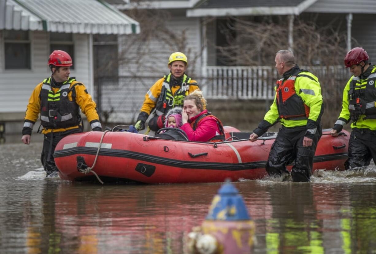 Firefighters use a raft to rescue Samantha Tucker, center, and her young child and infant, after rising flood waters submerged her home, Wednesday, Feb. 21, 2018, in South Bend, Ind.