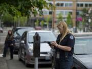 Parking enforcement officer Holly Naramore issues a ticket for an expired meter in downtown Vancouver in 2017. The city is now talking about increasing parking rates and developing demand-based fees.