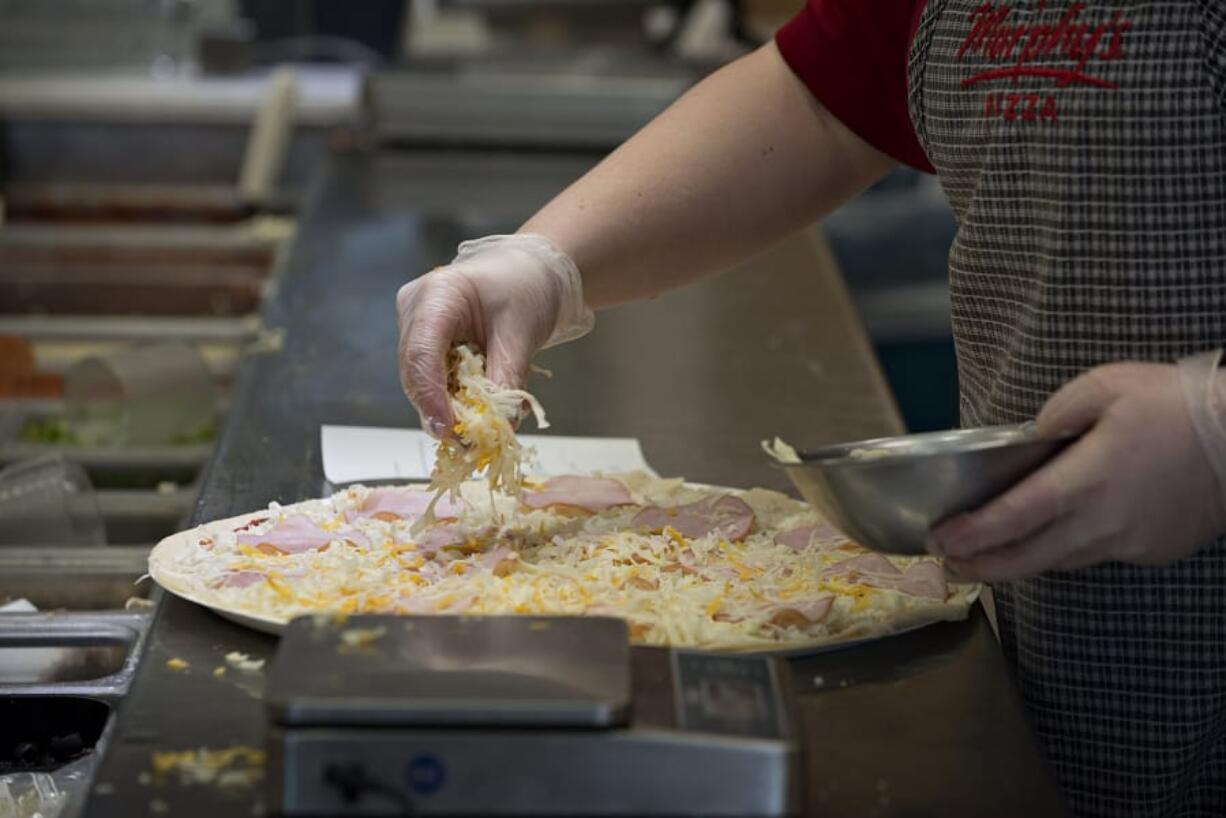 A Papa Murphy’s worker in Vancouver sprinkles cheese while creating a pizza. The Vancouver-headquartered company is hoping delivery and online ordering can help return it to profitability.