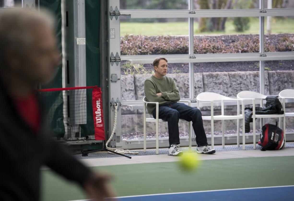 Camas’ Jason Hill watches his fellow tennis league members warm up at Evergreen Tennis Wednesday. Hill came to visit the center for the first time since his heart attack there Feb. 28, and he feels strongly were it not for them, he wouldn’t have survived.