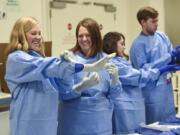 Washington State University medical students Morgan Black, 26, of Spokane, left, and Megan Short, 27, of Vancouver, laugh as Black attempts to properly put on her surgical glove during a workshop on gowning and gloving for the operating room. First-year medical students spent several hours Monday afternoon learning from the staff at Legacy Salmon Creek Medical Center. They’re in town all week.