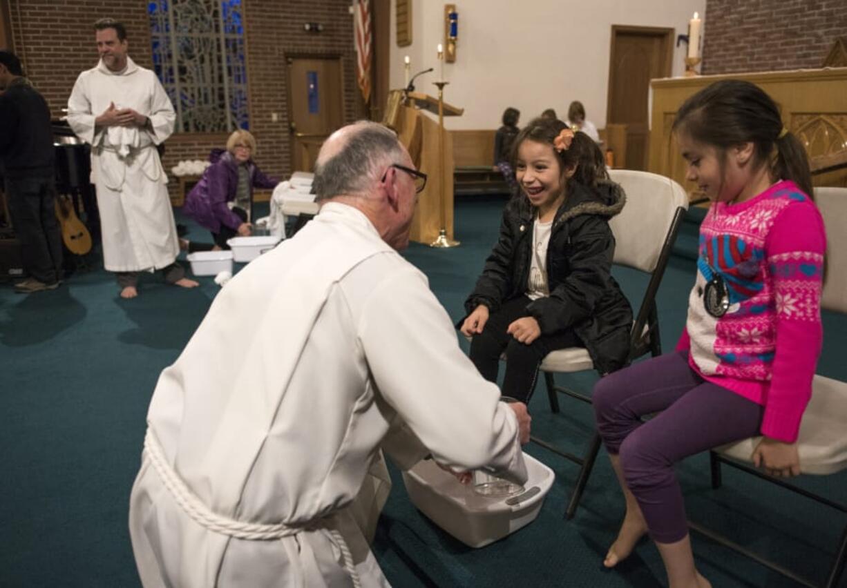 Caylin Orozco, 6, center, and Darisley Gonzales, 8, right, both of Vancouver, take a seat as the Rev. Dennis Cole, assistant rector, washes their feet during the Maundy Thursday service at St. Luke’s Episcopal Church. Foot washing is a hallmark of the holy day commemorating the Last Supper.