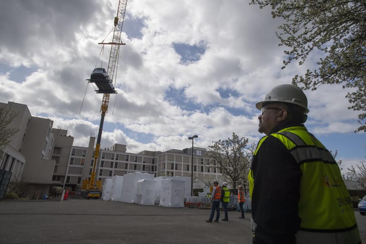 Bobby Blanks, safety manager for Howard S. Wright Construction, looks on as a crane lifts a Kia Soul over a building at PeaceHealth Southwest Medical Center. The vehicle, donated by Dick Hannah Kia, was placed on a third-floor outdoor patio and will be used by rehabilitation patients learning how to enter and exit a vehicle.