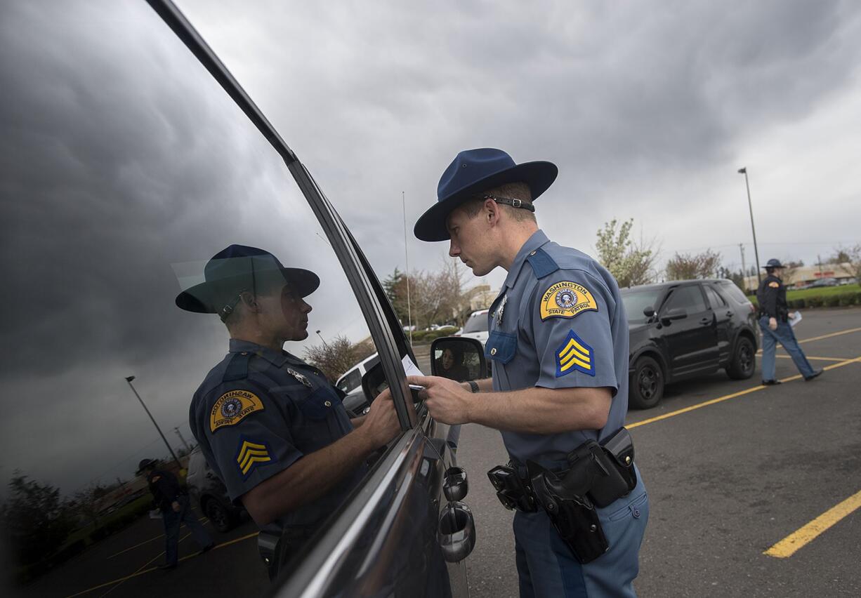 Sgt. Jason Cuthbert of the Washington State Patrol is reflected in the window of a car as he issues an infraction for distracted driving in southeast Vancouver in April.