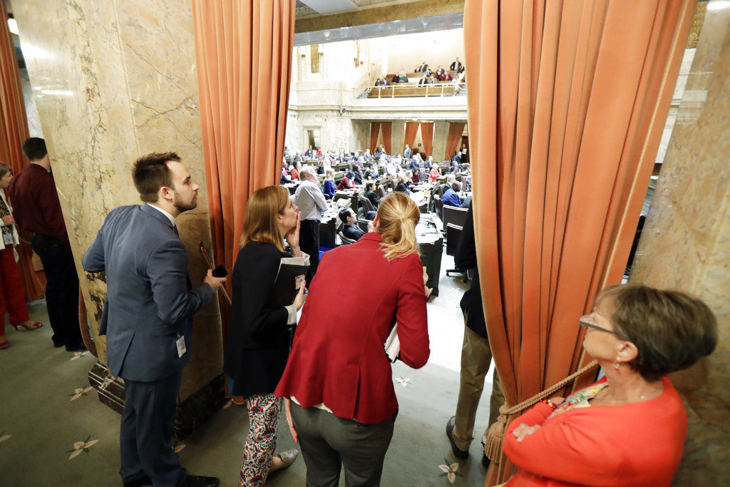 Legislative staffers watch from the wings of the House as votes are tallied, Thursday, March 8, 2018, at the Capitol in Olympia, Wash., on the final day of the regular session of the Legislature. The House on Thursday passed a supplemental budget plan that puts more money toward teacher salaries this year, the final step in a multiyear process to bring Washington into compliance with a state Supreme Court mandate on education. (AP Photo/Ted S.