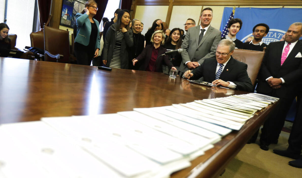 A long line of bills are placed on a table in the Governor's conference room at the Capitol in Olympia, Wash., Wednesday, March 21, 2018, as Washington Gov. Jay Inslee, center right, begins a signing ceremony. Among other measures, Inslee signed a package of bills meant to address sexual misconduct at the workplace in the wake of a national conversation about sexual harassment sparked by the #MeToo movement. (AP Photo/Ted S.