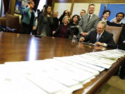 A long line of bills are placed on a table in the Governor's conference room at the Capitol in Olympia, Wash., Wednesday, March 21, 2018, as Washington Gov. Jay Inslee, center right, begins a signing ceremony. Among other measures, Inslee signed a package of bills meant to address sexual misconduct at the workplace in the wake of a national conversation about sexual harassment sparked by the #MeToo movement. (AP Photo/Ted S.