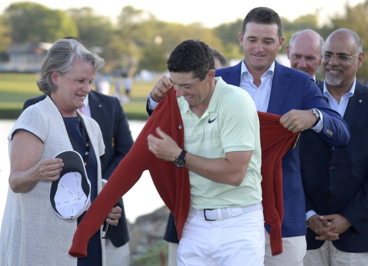 Rory McIlroy, of Northern Ireland, gets help putting on the championship sweater by Arnold Palmer’s grandson, Sam Saunders, right, and his widow, Kit Palmer, left, after winning the Arnold Palmer Invitational golf tournament Sunday, March 18, 2018, in Orlando, Fla. (AP Photo/Phelan M.