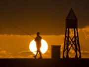 FILE - In this July 14, 2016, file photo, a fisherman prepares to cast a line as the sun rises behind him as he fishes off a jetty into the Atlantic Ocean, in Bal Harbour, Fla. Florida will join most of the nation Sunday, March 11, 2018, in springing ahead, moving clocks up one hour to observe daylight saving time. If Sunshine State legislators get their way, there soon will be no falling back.