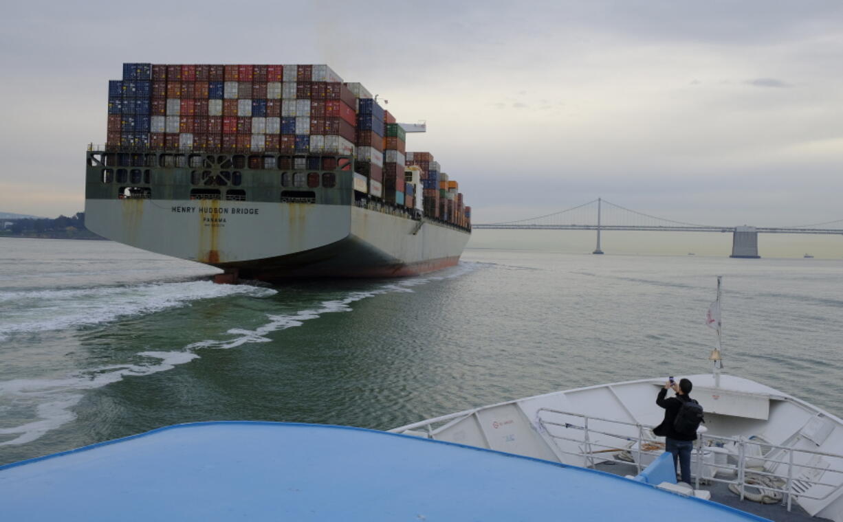 FILE- In this March 7, 2018, file photo, a man standing on the bow of a Golden Gate Ferry takes a picture of a container ship as it heads toward the San Francisco-Oakland Bay Bridge in San Francisco. On Wednesday, March 28, the Commerce Department issues its final estimate of how the U.S. economy performed in the October-December quarter.