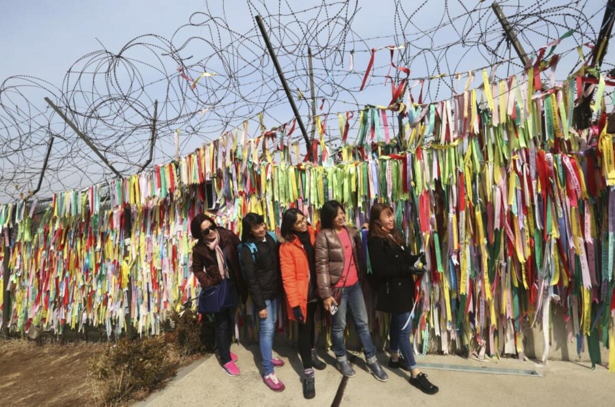 Visitors pose in front of ribbons placed on a barbed wire fence with messages wishing for the reunification of the two Koreas at the Imjingak Pavilion in Paju, near the border with North Korea, South Korea, on Wednesday. The meeting between North Korean leader Kim Jong Un and South Korean envoys marked the first time South Korean officials have met with the young North Korean leader in person since he took power after his dictator father’s death in late 2011. It’s the latest sign that the Koreas are trying to mend ties after one of the tensest years in a region that seems to be permanently on edge.